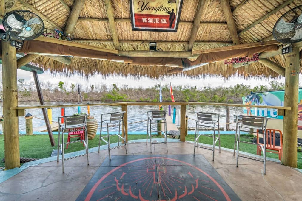 Wooden bar with bar stools looking over water under a large tiki roof at Miceli's restaurant.