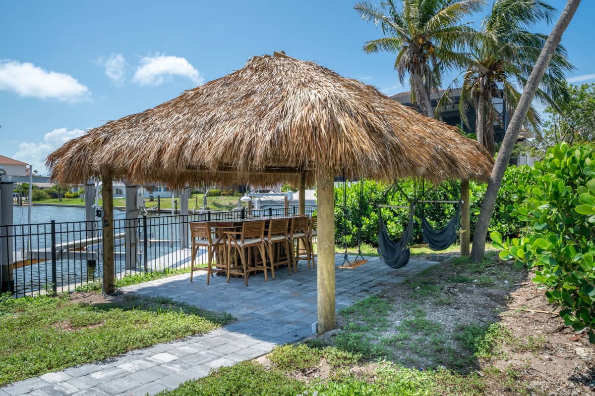 Waterside tiki built at the end of a paver path with swings and hammocks suspended by the structure.
